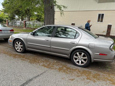 A silver 2002 Nissan Maxima parked on the side of the road featuring four doors and alloy wheels