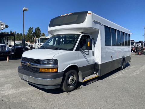 A 2020 Chevrolet Express is parked with a white exterior, large windows, and a low step at the entrance, designed for passenger transport