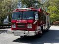 A 2006 Emergency One Fire Truck with a bright red exterior featuring the words Fire Dept on the front and multiple lights and equipment on top and sides