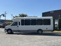 A 2017 Chevrolet Express bus with a white exterior and large windows parked on a gravel surface