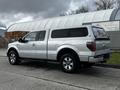 A silver 2014 Ford F-150 pickup truck with an extended cab and a camper shell on the bed parked on a street