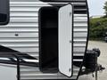 A 2021 Jayco Jay Flight travel trailer showing a side entry door that opens to a storage compartment with black and silver striped exterior design