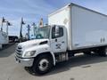 A 2018 Hino 338 box truck with a white body and chrome front grille parked with a side view showcasing its large cargo space