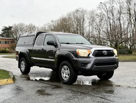 A 2015 Toyota Tacoma in gray with a truck bed cover parked on a wet surface featuring rugged wheels and a sturdy design