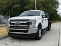 A white 2020 Ford F-350 with a flatbed, chrome grille, and prominent headlights parked on a paved surface