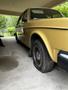 A 1978 Volvo 244 in yellow with a flat tire parked under a shelter