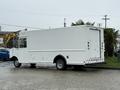 A white 2012 Ford Econoline delivery truck with a blank cargo area and rear roll-up door parked on a wet surface