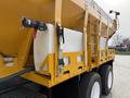 A yellow International 7600 truck with a large, mounted container on its side featuring a hose attachment and safety straps for secure storage
