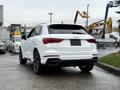 A white 2024 Audi Q3 with a sleek design and sporty rear end is parked showing its distinctive tail lights and dark wheels