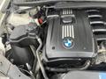 Engine compartment of a 2011 BMW 3-Series featuring a black engine cover with BMW logo and silver stripes detailing