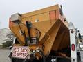 A yellow 2012 International WorkStar equipped with a large salt hopper and warning signage including a keep back 20 meters notice
