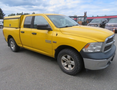 A yellow 2015 RAM 1500 pickup truck with a truck cap on the bed parked on a gravel surface
