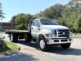 A 2008 Ford F-750 flatbed truck with a silver exterior and a black flatbed is seen from the front angle showcasing its large grille and headlights