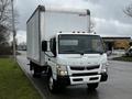 A 2021 Mitsubishi FE truck with a boxy cargo area painted white and a front with multiple orange lights across the top