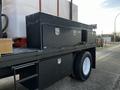 A 2011 Ford F-750 truck with a flatbed featuring several black toolboxes secured to the frame and a large white water tank mounted in the rear