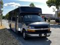 A 2019 Chevrolet Express bus with a black front, silver body, and large windows parked on the side of a road