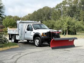 A 2007 Ford F-450 truck equipped with a red snow plow in the front and a utility bed in the back
