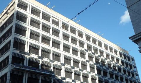 A multi-story building undergoing structural repair with scaffolding visible and exposed concrete walls and window frames