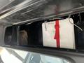 An overhead storage compartment in a 2007 Freightliner B2 containing a white container secured with a red strap and a piece of paper labeled with a number
