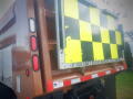 A 2016 International WorkStar 7500 truck with a brown body and yellow and black checkerboard pattern on the rear panel featuring a safety message
