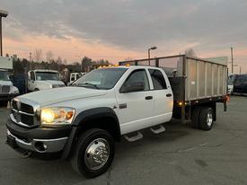 A 2008 Dodge Ram 5500 with a white exterior and a dump bed in the back parked on a lot with its headlights on