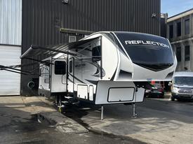 A 2021 Grand Design Recreational 311BHS travel trailer with a sleek white exterior featuring the word REFLECTION on the front and a retractable awning on the side