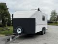 A white and black 2025 Shuttle Office trailer with double axles and a rounded top design parked on a smooth surface