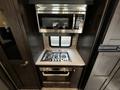 A modern kitchenette featuring a stainless steel microwave above a gas cooktop with five burners and a built-in oven below in a 2021 Grand Design Recreational 311BHS
