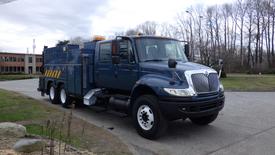 A blue 2007 International 4400 truck with a utility body and orange lights on the roof parked on a driveway