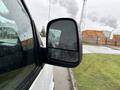 A side view mirror of a 2014 GMC Savana van with water droplets on it and a blurred reflection visible in the mirror