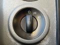 A black control knob labeled with symbols for headlights and parking lights on a textured gray surface
