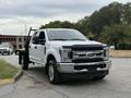 A 2019 Ford F-350 Super Duty truck with a white exterior and chrome accents parked at an angle with a flatbed attachment and shiny wheels