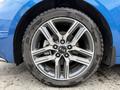 A close-up of a silver alloy wheel on a blue 2021 Kia Forte showing five spokes and a black tire with tread pattern