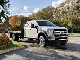 A 2019 Ford F-550 truck with a flatbed design featuring a chrome grille and a cab with a light bar on top