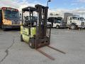 A 2000 Clark GPS 15 forklift with a yellow and green body and extended lifting forks in the foreground