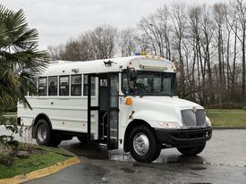 A white 2016 International CE300 school bus with an open door and side lights on, showcasing its large front grille and windows