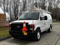 A white 2011 Ford Econoline van with a ladder rack on top and traffic cones mounted on the front grille