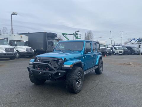 A 2020 Jeep Wrangler in a vibrant blue color featuring a front bumper guard and off-road tires parked in a lot