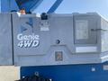 A 1997 Genie S-65 4X4 boom lift with a faded blue and gray exterior featuring the Genie logo and a control panel on the side