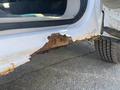 A rusted area on the lower edge of a white 2013 Ford Expedition door showing significant wear and corrosion on the metal