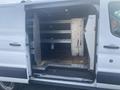 A 2017 Ford Transit van with its rear doors open revealing a spacious cargo area featuring metal shelves and a rubberized floor