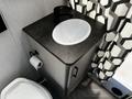 A countertop with a white sink and black faucet next to a toilet featuring a roll of toilet paper hanging on the side