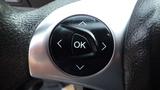 A steering wheel control button cluster featuring three directional arrows and a central OK button