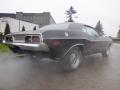 A 1974 Dodge Challenger with a sleek black exterior and chrome details emits smoke from the exhaust in a side view showcasing its classic muscle car design
