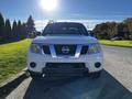 A 2015 Nissan Frontier in white facing forward with a prominent grille and logo visible