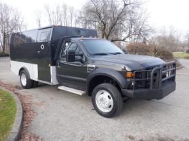 A 2009 Ford F-550 truck with a black armored shell and silver lower paneling parked on a concrete surface