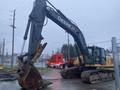 A 2014 John Deere 350G excavator with a large digging bucket positioned to the side and tracks visible on a concrete surface