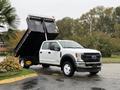 A 2022 Ford F-550 truck with a raised dump bed displaying a white exterior and black features in the foreground