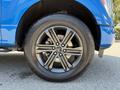Close-up of a black alloy wheel on a blue 2021 Ford F-150 showcasing five spokes and a large tire with visible tread patterns