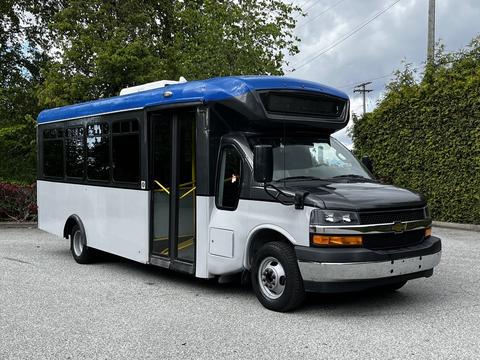 A 2019 Chevrolet Express bus with a black front and white body, featuring a blue roof and large windows on the side